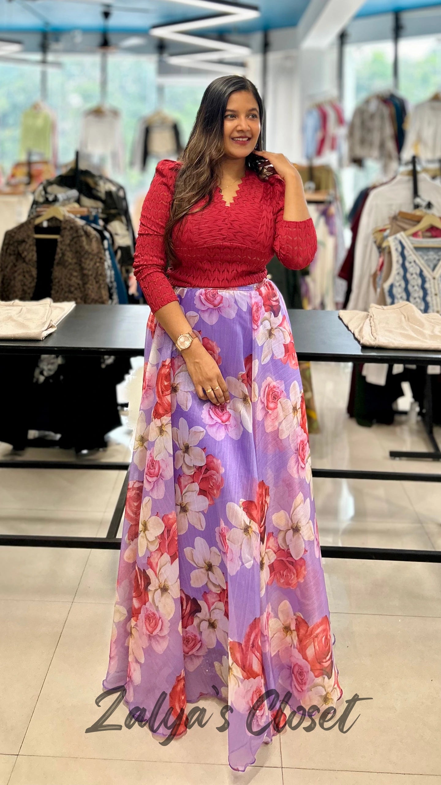 Woman wearing a red top and floral skirt in a clothing store.