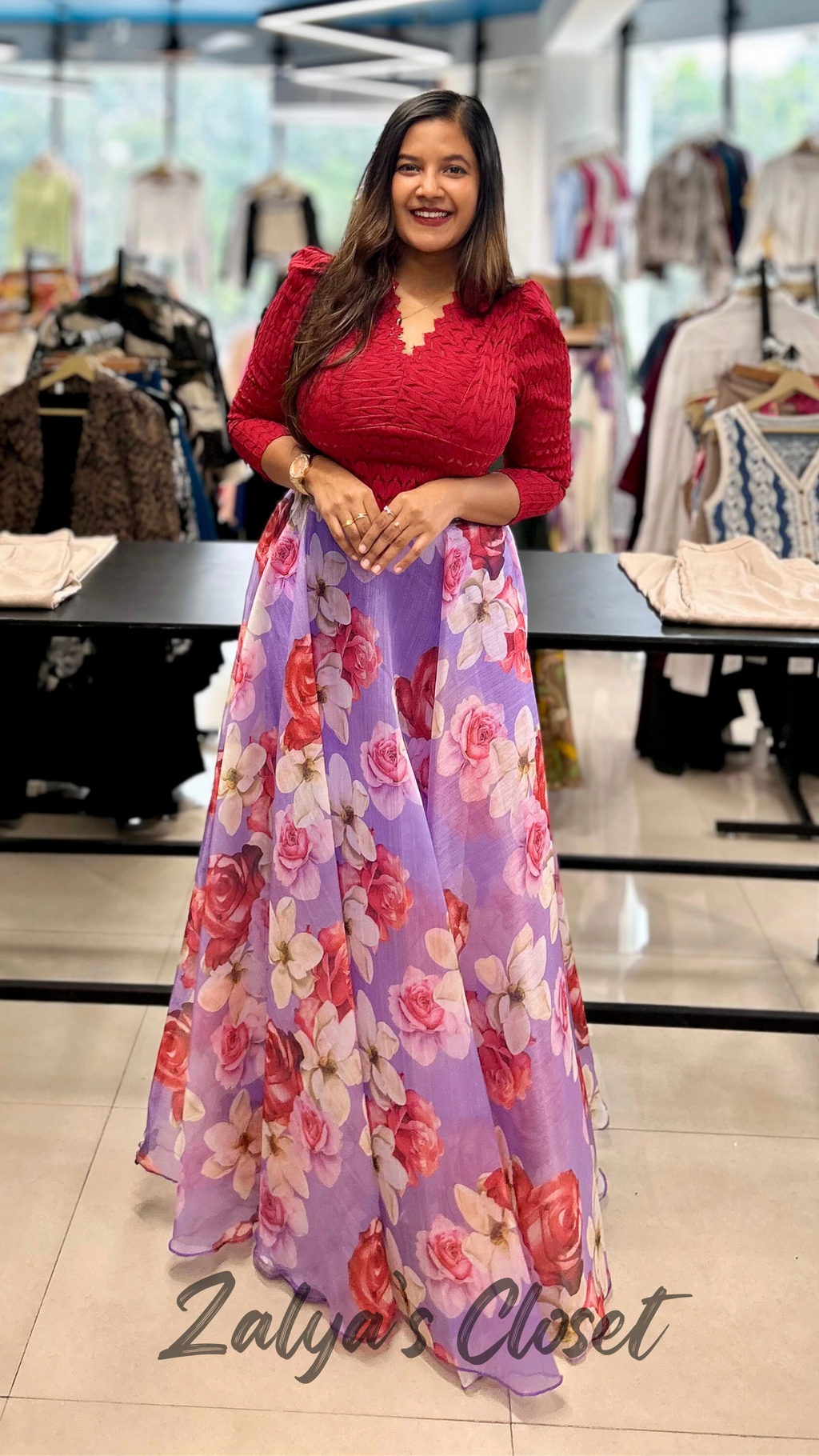 Woman wearing a red top and purple floral skirt in a clothing store.